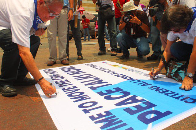 Bishop Deogracias Iñiguez (left) and Karen Tañada of Waging Peace Philippines sign the tarpaulin calling for resumption of GPH-NDFP peace talks. (Photo by Ronalyn V. Olea/ Bulatlat.com)