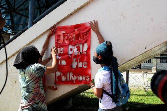 Protesters paint the words “Justice is dead in the Philippines” during the funeral caravan of Emerito Samarca.