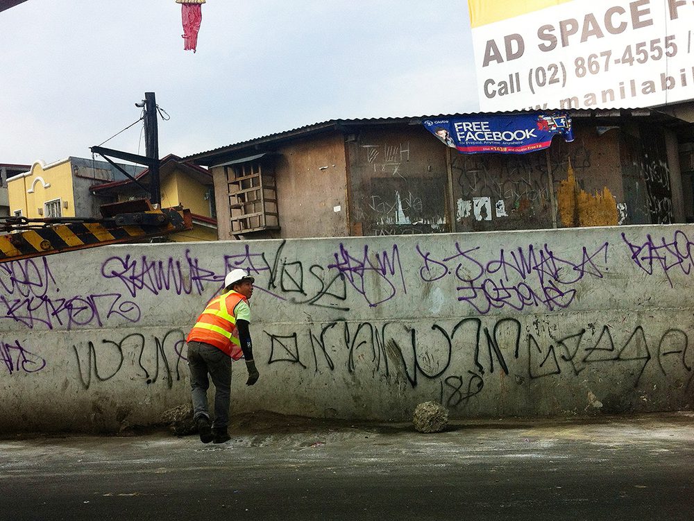 While other cities appear to be proud of their street art, a construction worker seem unconcerned with Manila's graffiti that no one seems to understand.  (Osmena Highway, Manila)