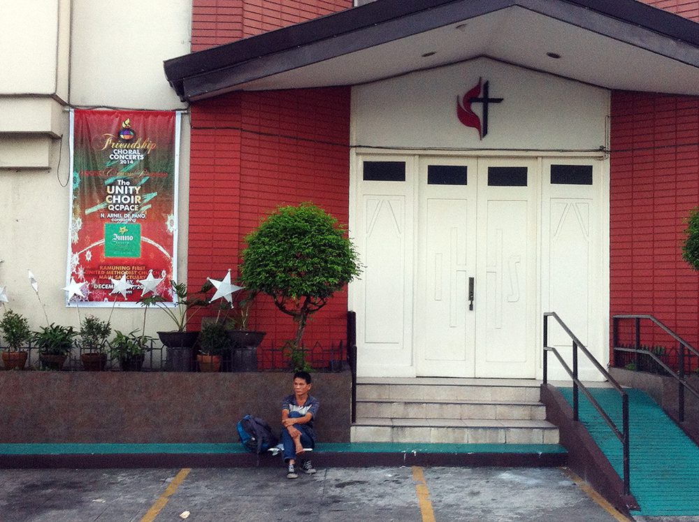 A man rests in front of a closed church building that appears to have already dispensed with Christmas celebrations. (Kamuning, Quezon City)
