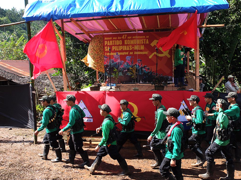 New People's Army fighters walk before their movement's standards as they take their positions for the start of the Communist Party's anniversary celebrations. (Kitcharao, Agusan del Norte)